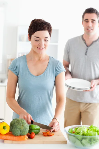 Женщина режет овощи и мужчина держит тарелки — стоковое фото