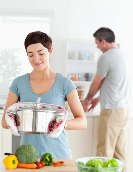 Ładny żona trzymając garnek, podczas gdy jej mąż jest zmywanie naczyń — Zdjęcie stockowe