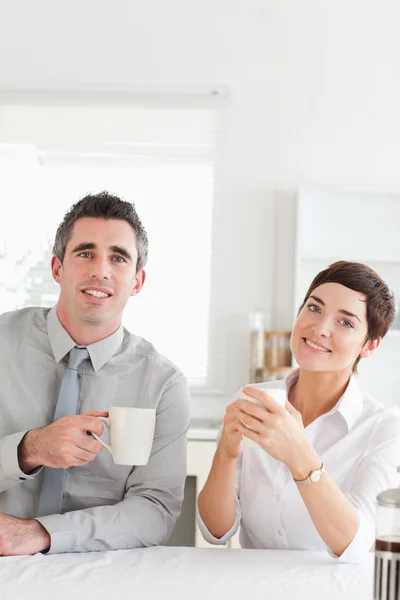 Smiling couple drinking coffee looking into the camera — Stock Photo, Image