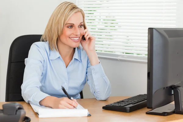 Cute blonde businesswoman on mobile writing something down looks Royalty Free Stock Photos