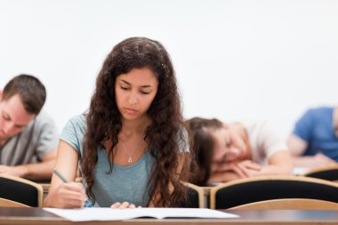 Students writing while their classmate is sleeping clipart