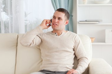 Young man on the phone while sitting on his couch clipart