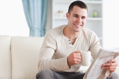 Happy man having a tea while reading the news clipart