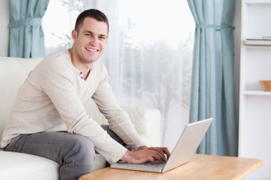 Smiling man typing on his laptop clipart