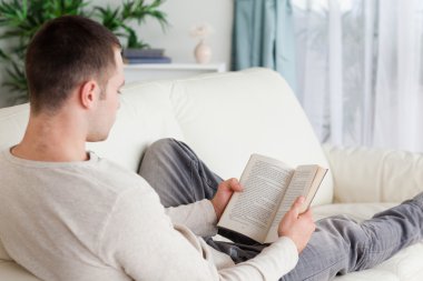 Portrait of a man lying on his couch reading a book clipart