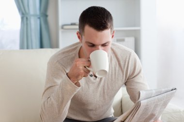 Young man reading the news while having a coffee clipart