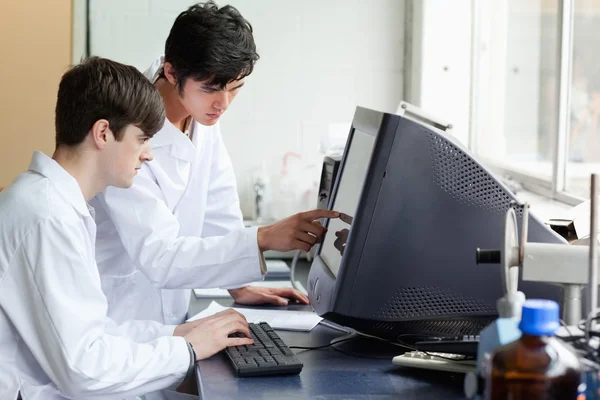Chemiker zeigt seinem Kollegen auf etwas auf einem Monitor — Stockfoto