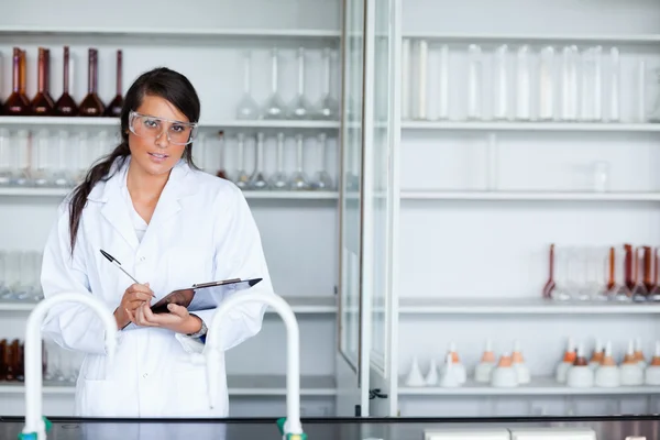 Cute female scientist writing on a clipboard — Stock Photo, Image