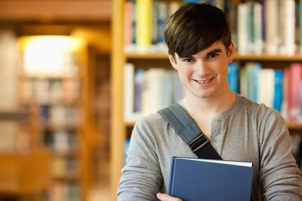 Uśmiechający się młody student trzyma książkę — Zdjęcie stockowe