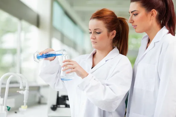 Cute scientists pouring liquid in an Erlenmeyer flask — Stock Photo, Image