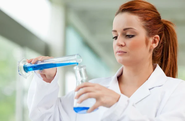 Junge Wissenschaftlerin gießt blaue Flüssigkeit in Erlenmeyerkolben — Stockfoto