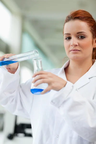 Porträt eines niedlichen Wissenschaftlers, der blaue Flüssigkeit in einen Erlenmeye gießt — Stockfoto