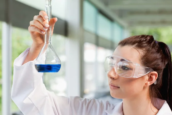 Junge Studentin der Naturwissenschaften blickt auf eine blaue Flüssigkeit — Stockfoto