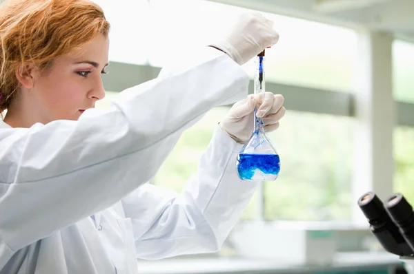 Estudante de ciências bonito colocando gotas azuis em um líquido — Fotografia de Stock