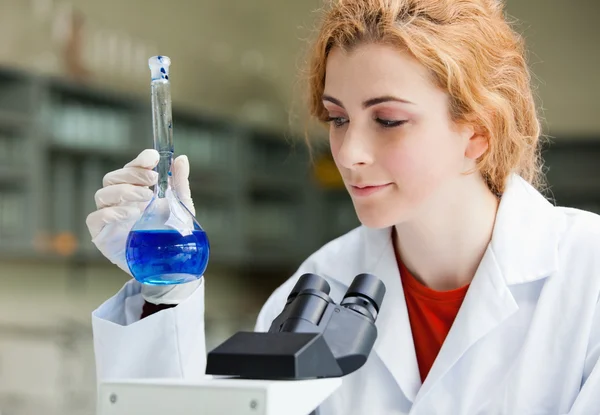 Smiling student looking at a blue liquid — Stock Photo, Image