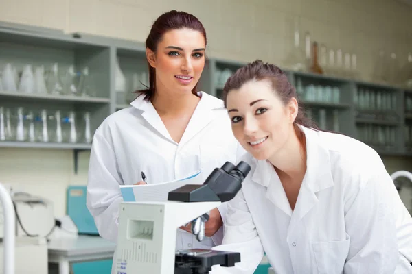 Estudantes de ciências bonitos posando com um microscópio — Fotografia de Stock