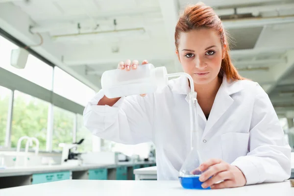 Red-haired scientist pouring liquid in a flask — Stock Photo, Image
