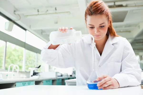 Red-haired focused scientist pouring liquid in a flask — Stock Photo, Image