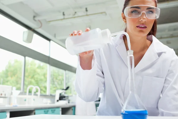 Mujer estudiante de ciencias vertiendo líquido con gafas protectoras —  Fotos de Stock