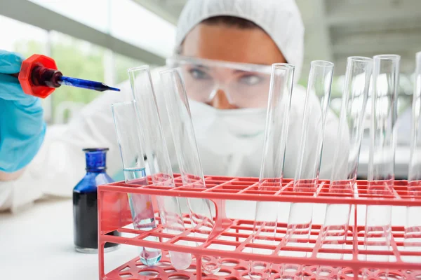 Protected female scientist dropping blue liquid in a test tube — Stock Photo, Image