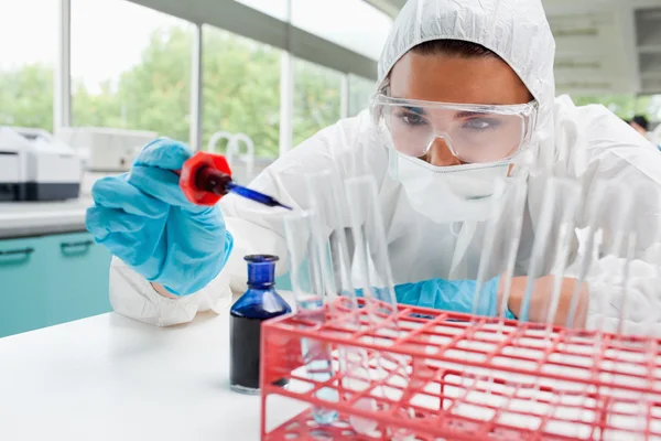 Protected cute female scientist dropping blue liquid in a test t — Stock Photo, Image