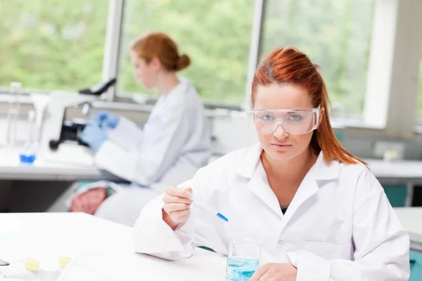 科学专业的学生在一个烧杯中滴蓝色的液体 — 图库照片