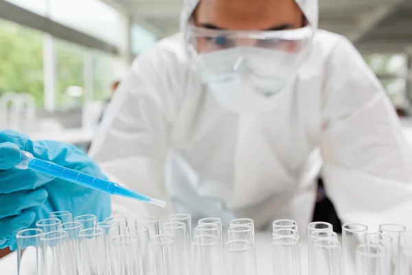 Protected scientist dropping a blue liquid in a test tube — Stock Photo, Image