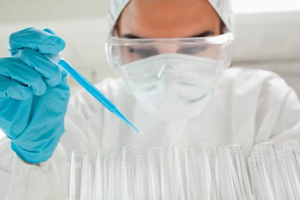 Cientista feminina protegida a deixar cair um líquido azul num tubo de ensaio — Fotografia de Stock
