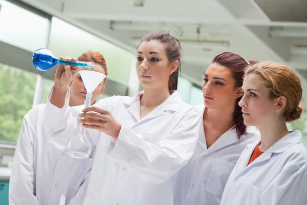 Female science students pouring liquid in a flask — Stock Photo, Image