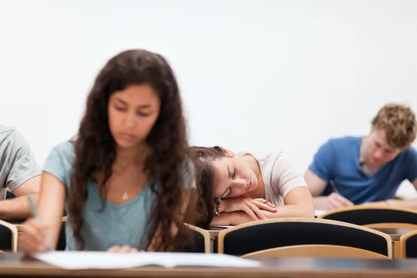 Studenti che lavorano mentre il loro compagno di classe sta dormendo — Foto Stock
