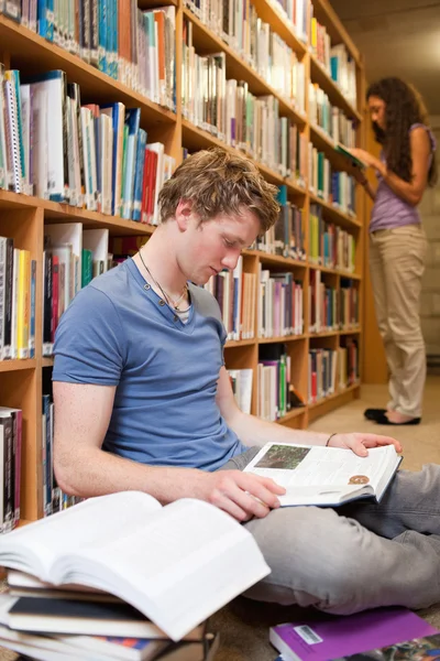 Retrato de un estudiante masculino leyendo libros mientras su compañero de clase es —  Fotos de Stock