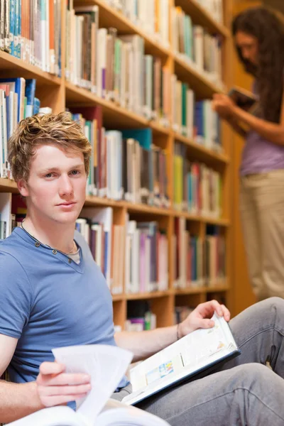 Porträt eines hübschen Studenten, der mit einem Buch posiert, während seine Klassenkameraden — Stockfoto