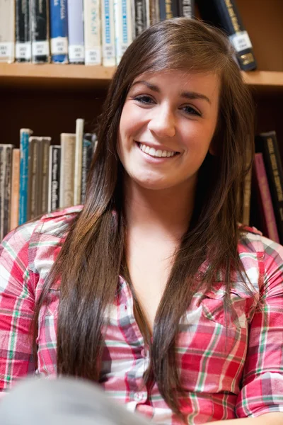 Porträt einer lächelnden Studentin, die vor Regalen sitzt — Stockfoto