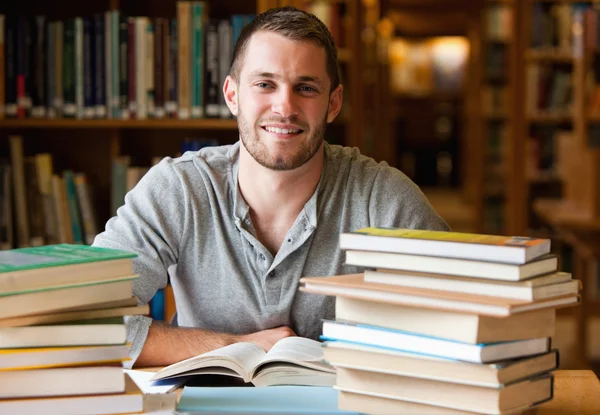 Улыбающийся студент в окружении книг — стоковое фото