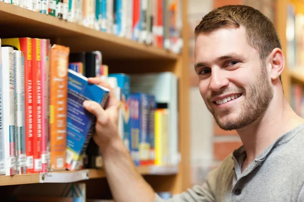 Sorridente studente maschio raccogliendo un libro — Foto Stock