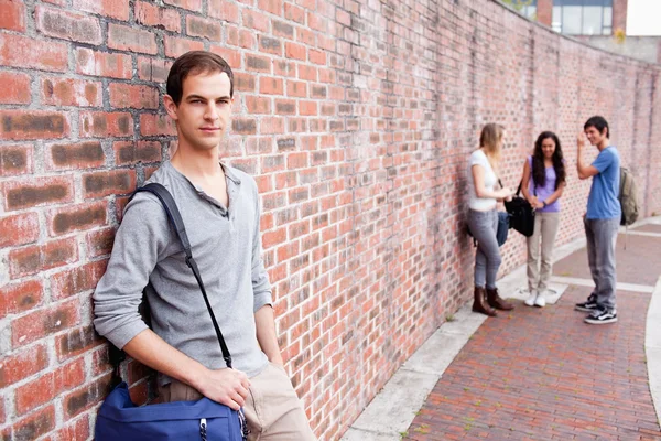 Student leaning on a wall while his friends are talking — Stock Photo, Image