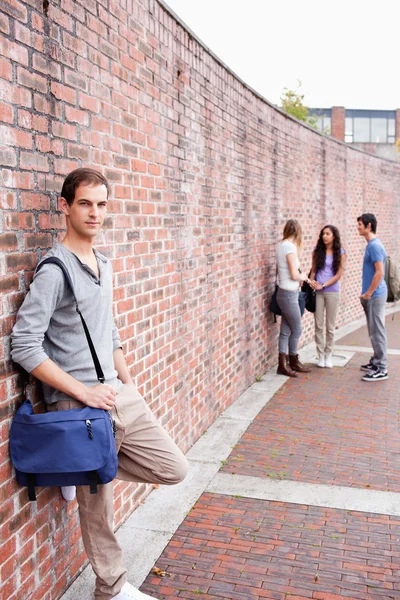 Porträt eines Studenten, der sich an eine Wand lehnt, während seine Freunde reden — Stockfoto
