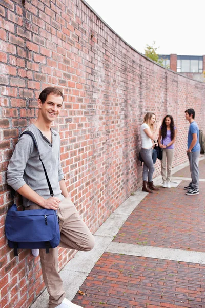 Portret van een mannelijke student leunend op een muur, terwijl zijn vrienden zijn praten — Stockfoto