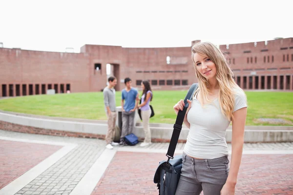 Студентка-блондинка позирует, пока ее друзья говорят — стоковое фото