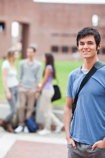 Porträt eines gutaussehenden Studenten, der posiert, während seine Klassenkameraden reden — Stockfoto