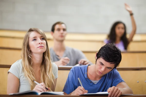 Estudiantes tomando notas mientras su compañera de clase levanta la mano —  Fotos de Stock