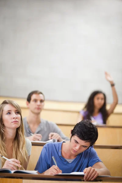 Retrato de estudantes tomando notas enquanto sua colega está levantando a mão — Fotografia de Stock