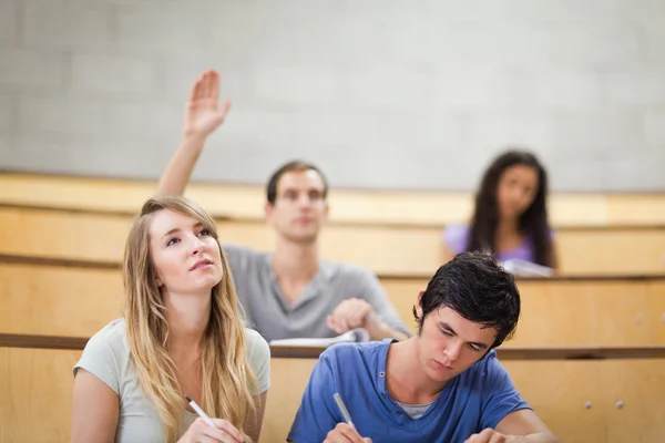Estudiantes tomando notas mientras su compañero de clase levanta la mano — Foto de Stock