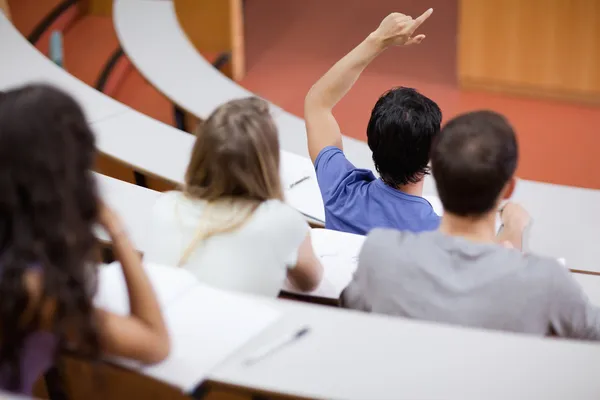 Молодой студент поднимает руку, пока его одноклассники делают заметки — стоковое фото