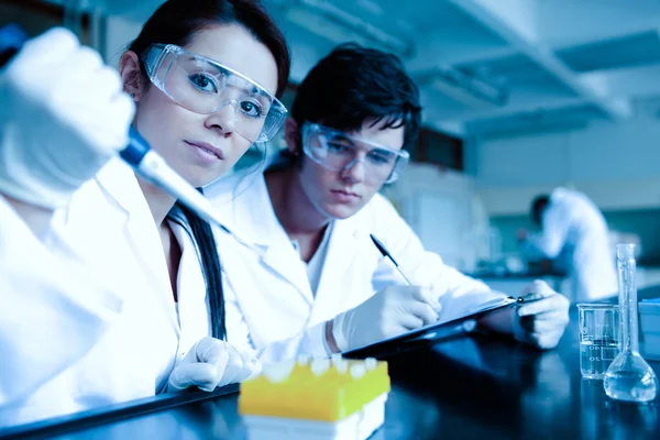 Estudante de ciência soltando líquido em tubos de ensaio, enquanto seu parceiro está tomando notas — Fotografia de Stock