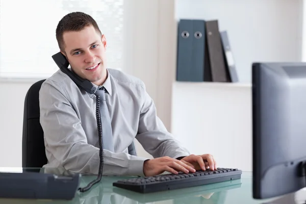 Negócio sorrindo no telefone e escrevendo em seu computador — Fotografia de Stock