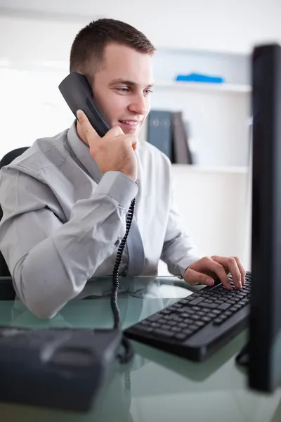 Businessman talking to costumer on the phone while using his com — Stock Photo, Image