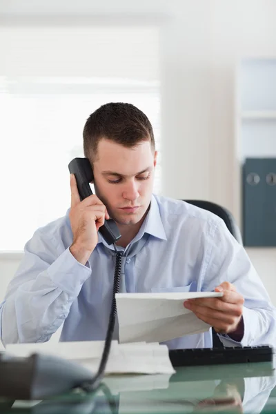 Close up of businessman looking at a letter while on the phone — Stock Photo, Image