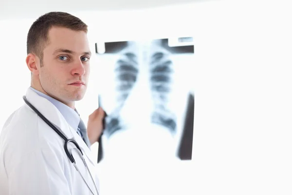 Médico de aparência séria segurando raio-X contra a luz — Fotografia de Stock