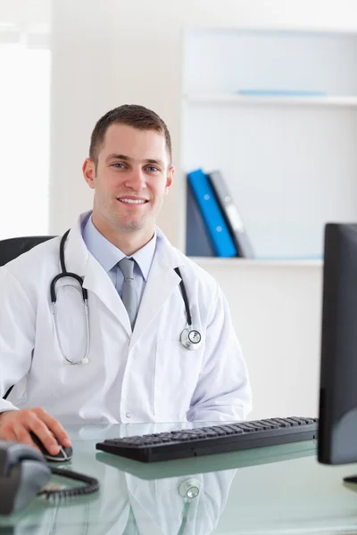 Uśmiechający się lekarz siedzi na swoim komputerze — Zdjęcie stockowe